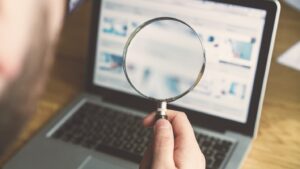 A person holds a magnifying glass over their laptop which shows a search engine.
