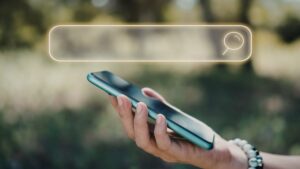 Person holding a smartphone with a glowing search bar above it, representing online search optimization across platforms.