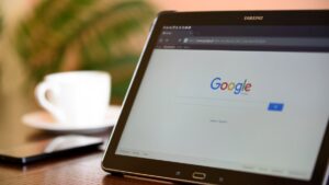 Tablet showing the Google search homepage on a table beside a coffee cup and smartphone